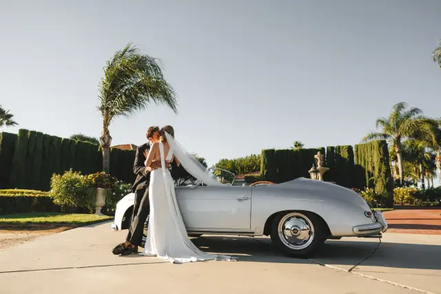 Newlyweds posing with a silver classic car at Villa de Amore